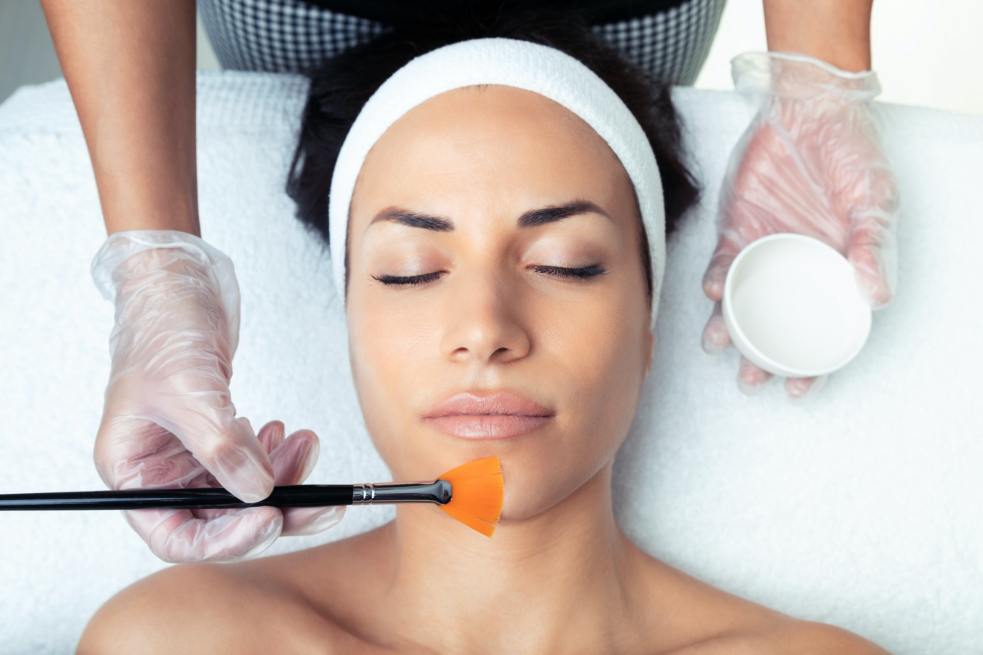 Cosmetologist making a chemistry peeling for rejuvenating the face to woman on the spa center.