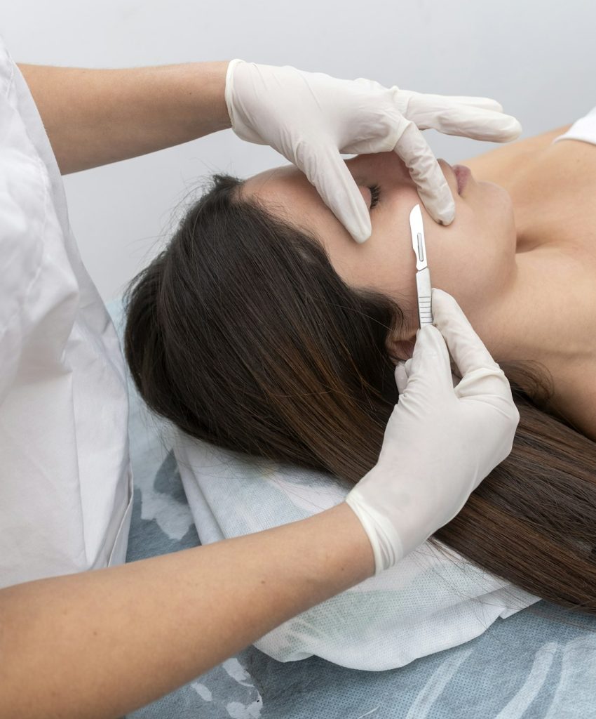 Vertical closeup of the doctor with a scalpel treating the woman's skin. Dermaplaning treatment.
